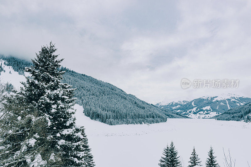 在白雪覆盖和冰冻的Speicher Durlassboden湖与松树和白雪覆盖的山脉